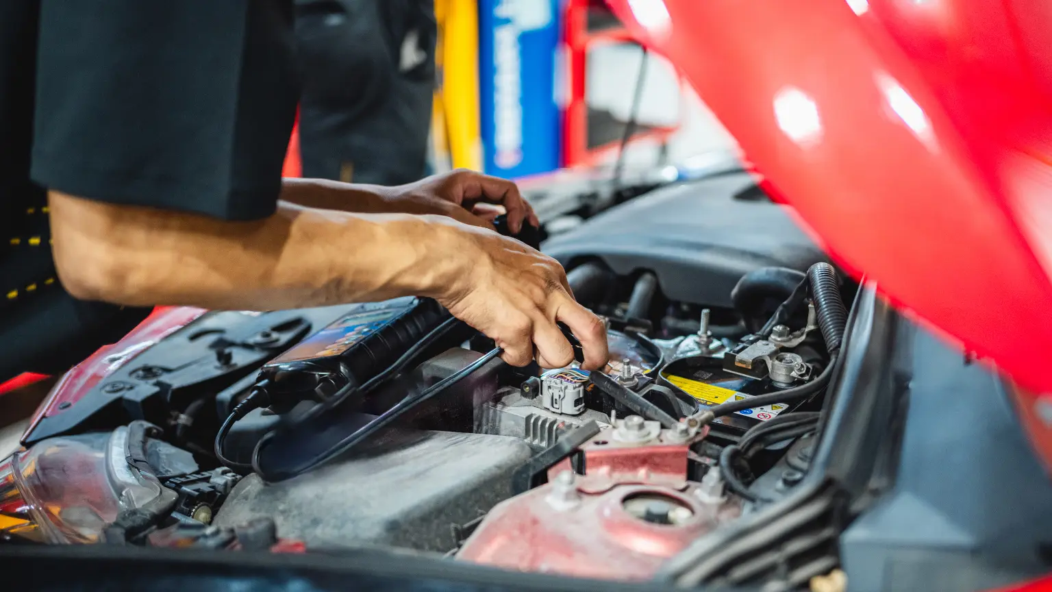 Automatic transmission issues being diagnosed by a technician using a diagnostic tool under a red car hood.