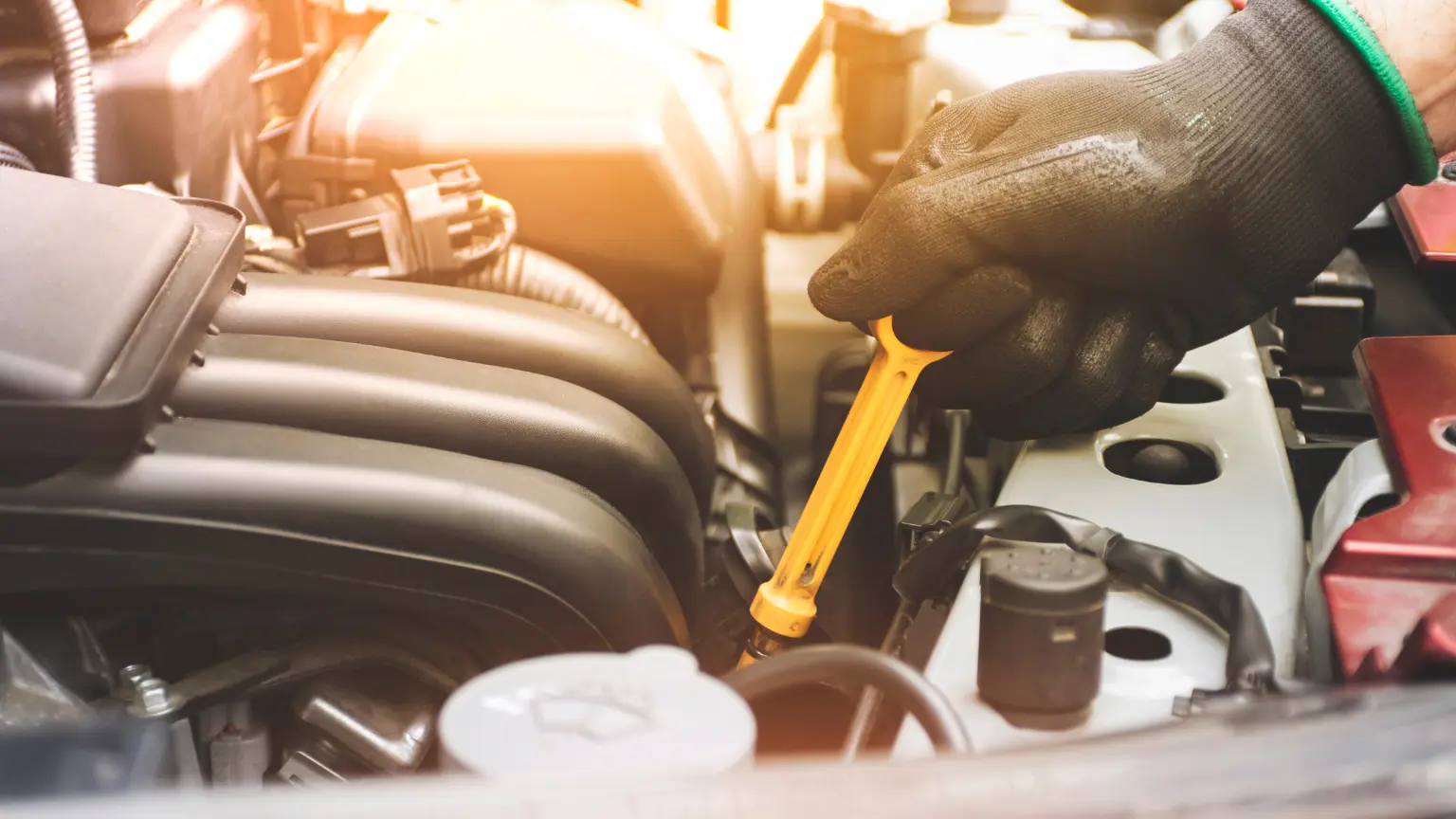 Transmission places offering service shown by a mechanic checking engine fluids with a yellow dipstick.
