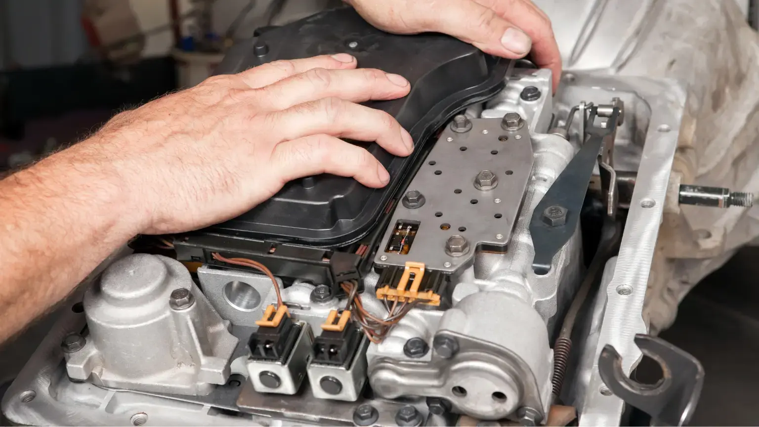 Transmission rebuild process showing hands working on valve body and electrical components of an automatic transmission.