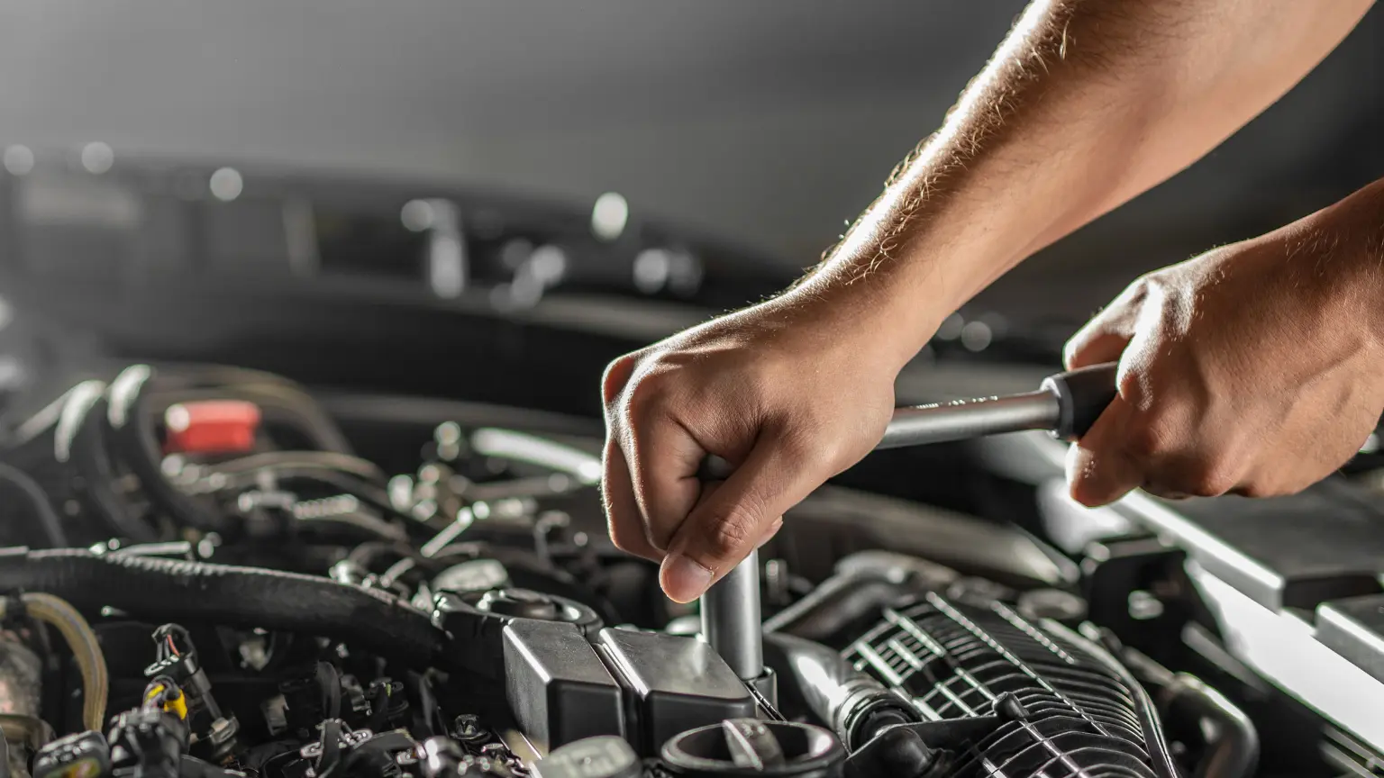 Transmission cooling maintenance shown by a mechanic tightening components inside an engine bay with a torque wrench.