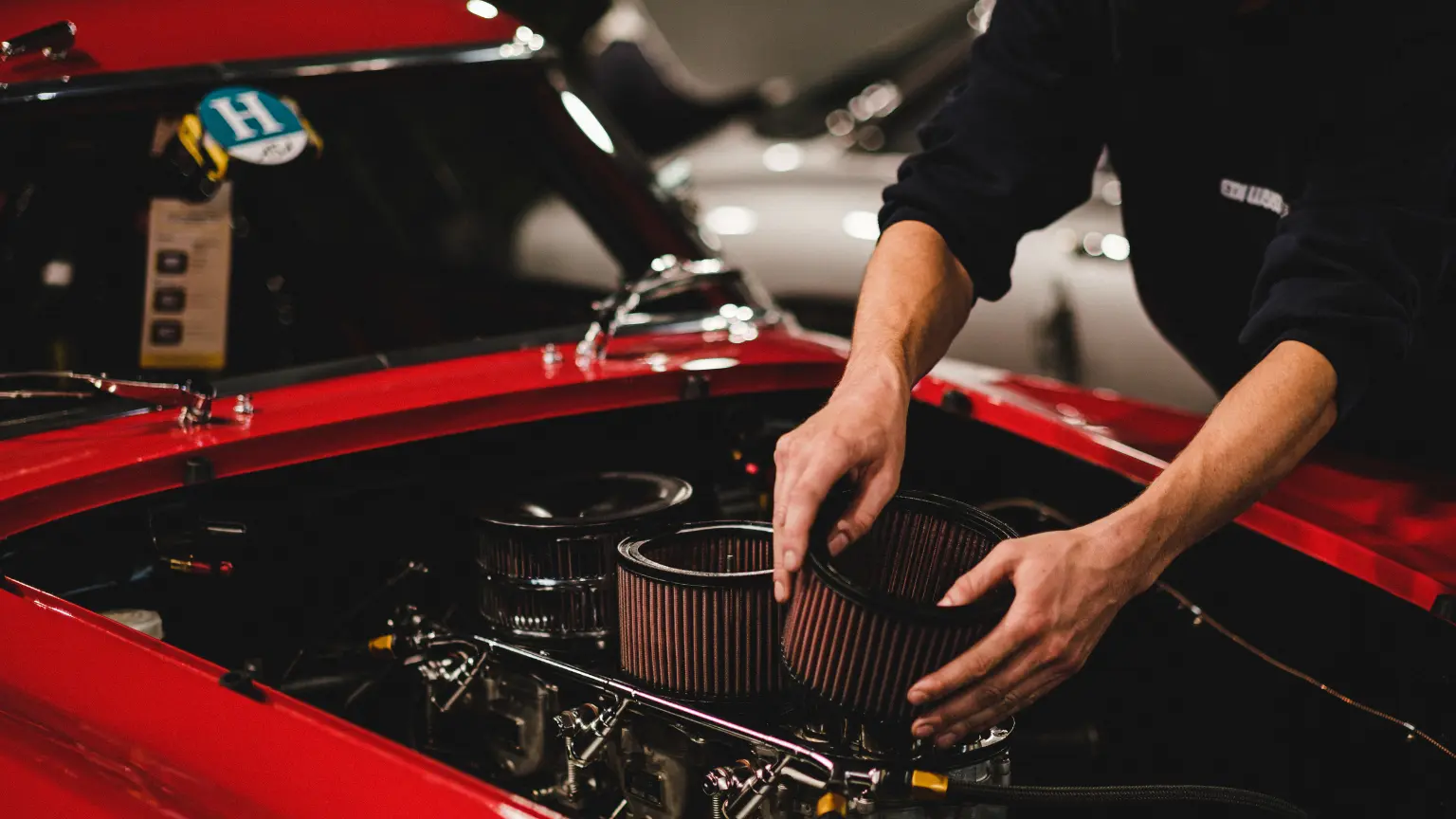 Transmission cooler inspection during engine maintenance as mechanic adjusts air filters in a classic red vehicle.