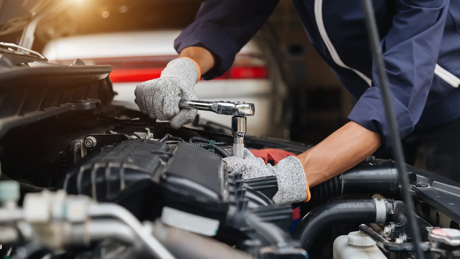 Transmission fluid service with mechanic using socket wrench on engine components wearing protective gloves.