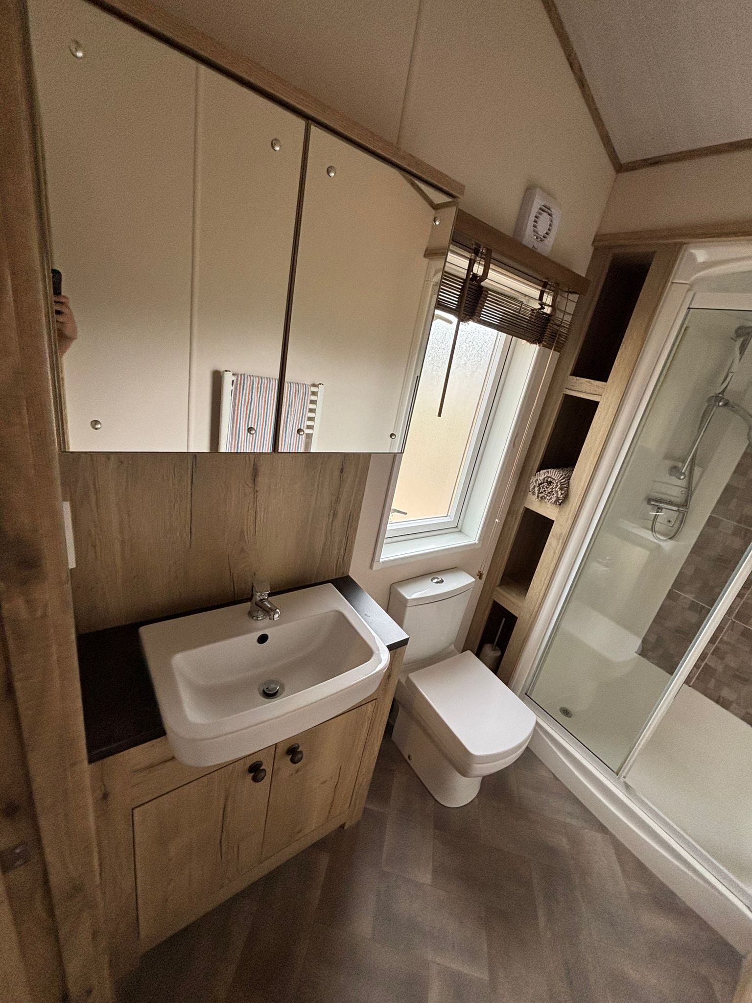 Modern bathroom with wooden accents, sink, toilet, and glass shower