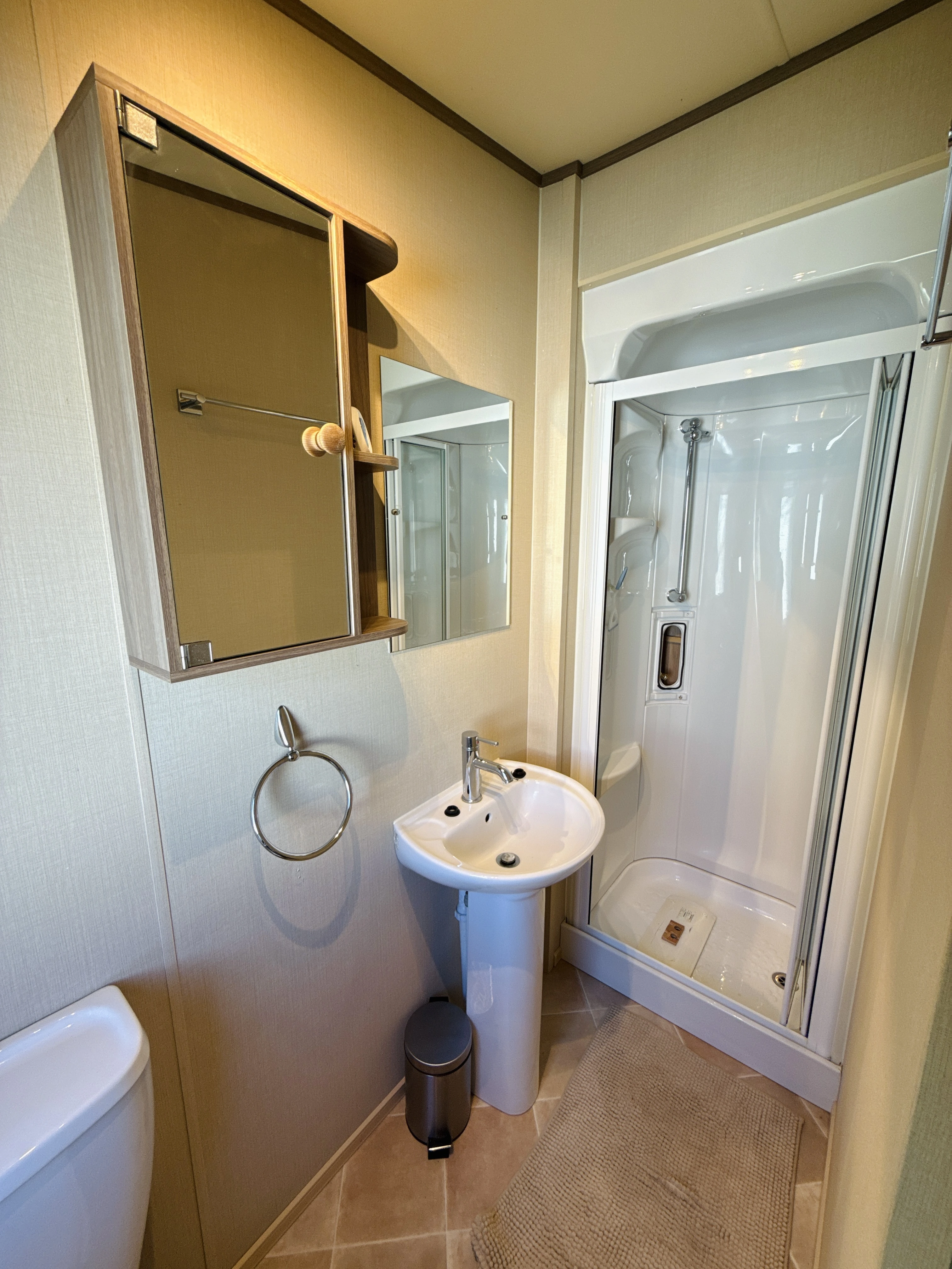 Compact bathroom with white shower, sink, mirror, and toilet