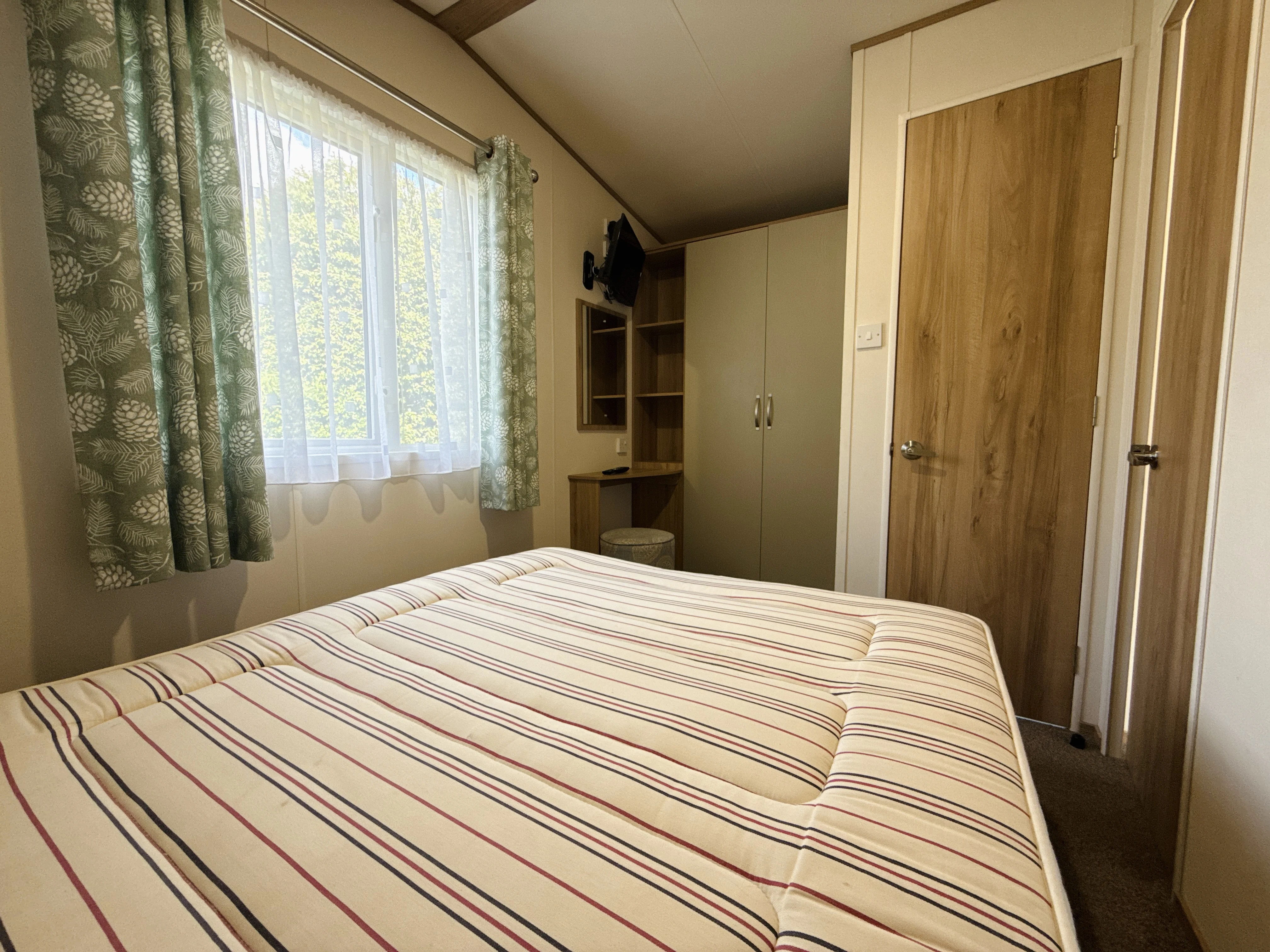 Cozy bedroom with striped bedding, green curtains, and wooden wardrobe