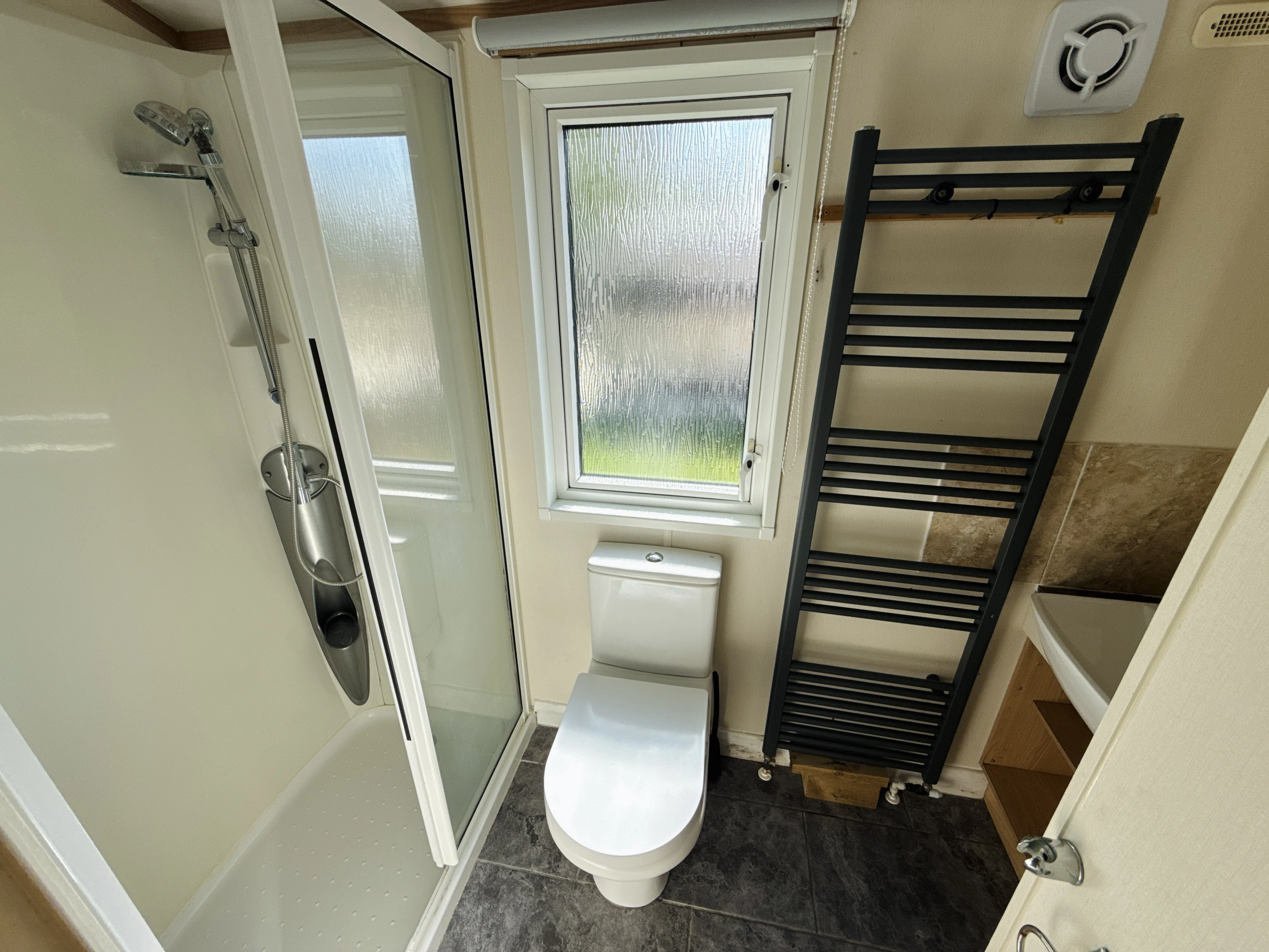Modern bathroom with shower, toilet, towel rack, and frosted window