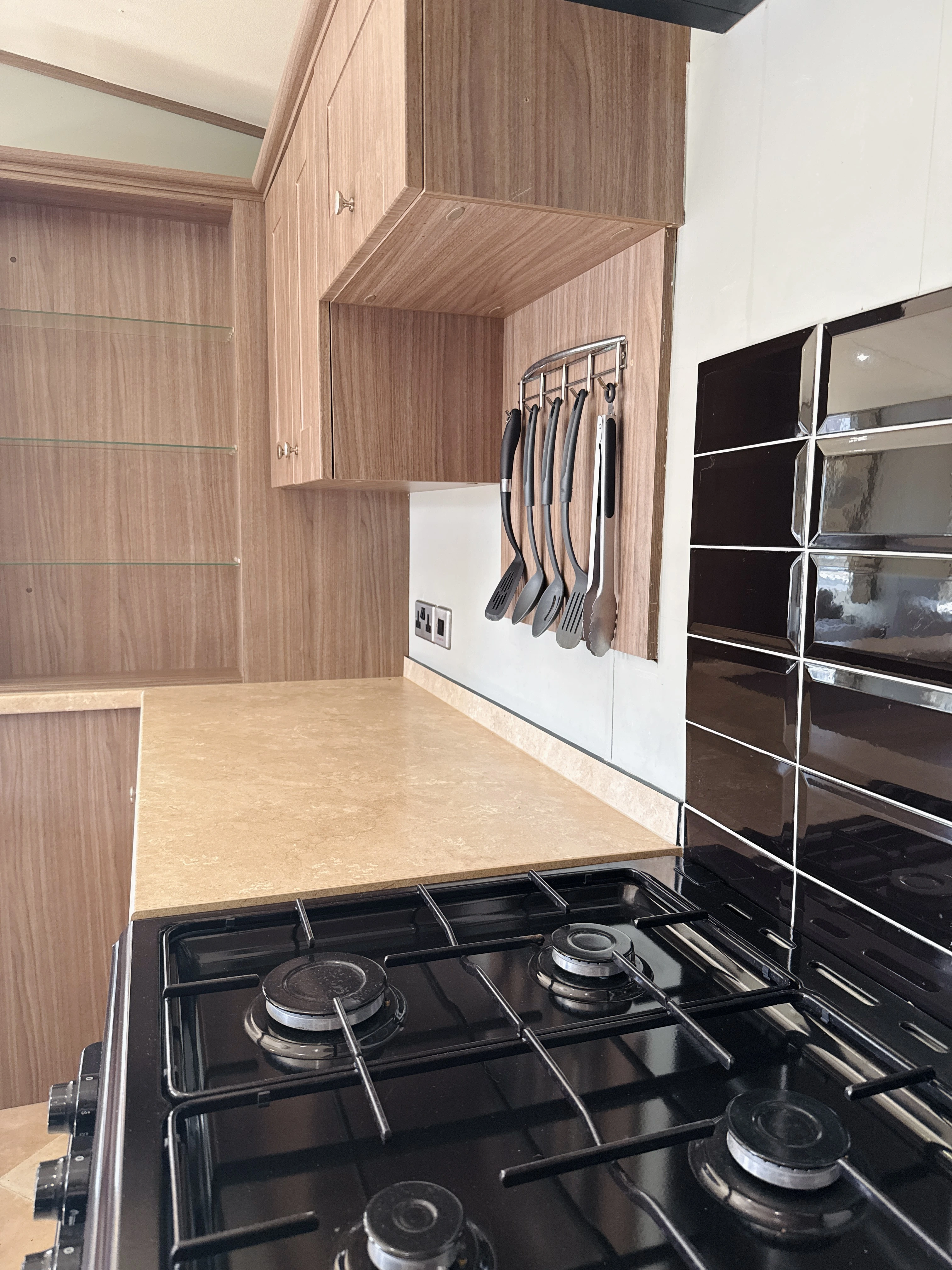 Modern kitchen with wooden cabinets, hanging utensils, and black gas stove