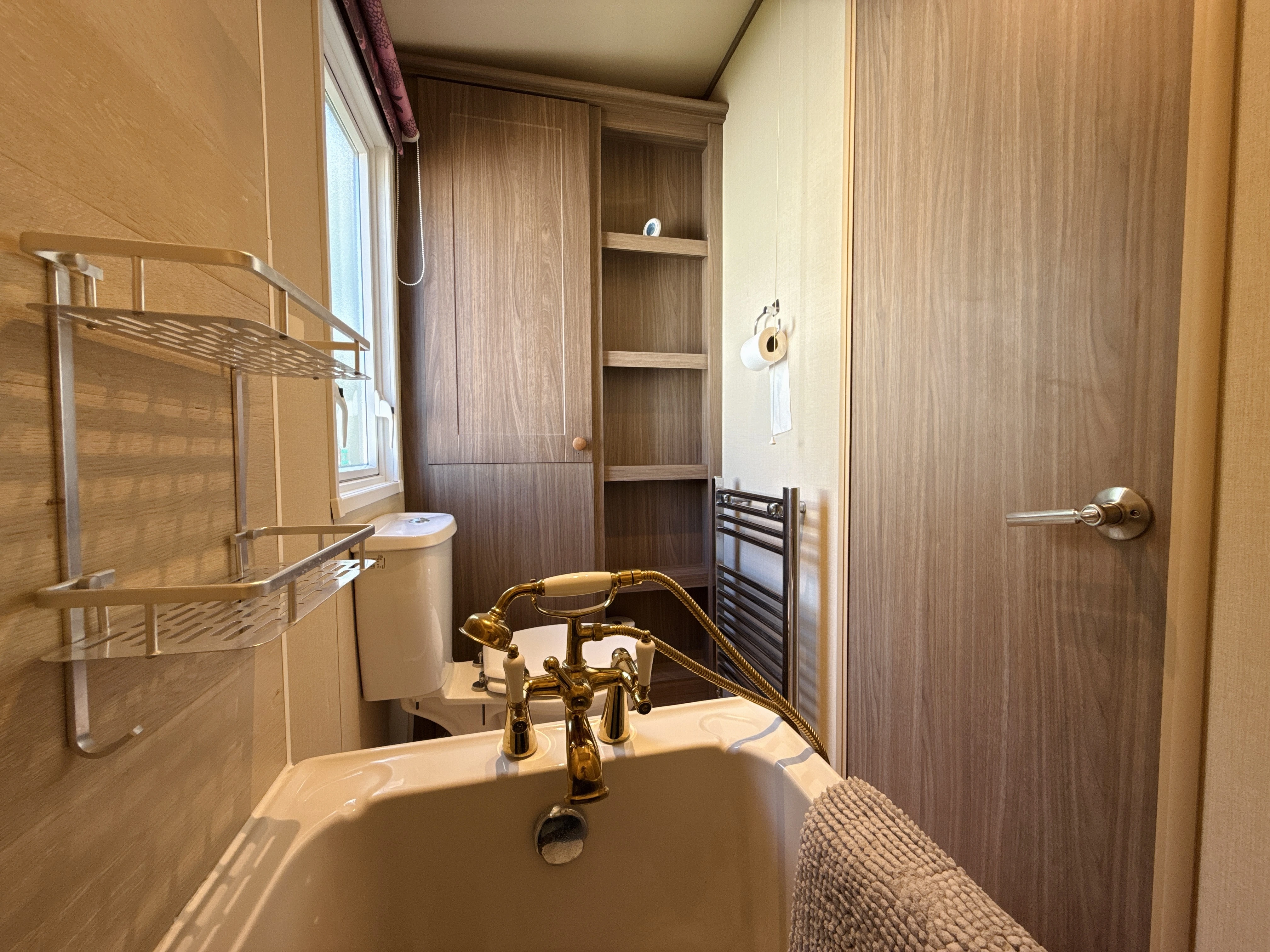 Wooden bathroom with bathtub, gold fixtures, built-in shelves, and window