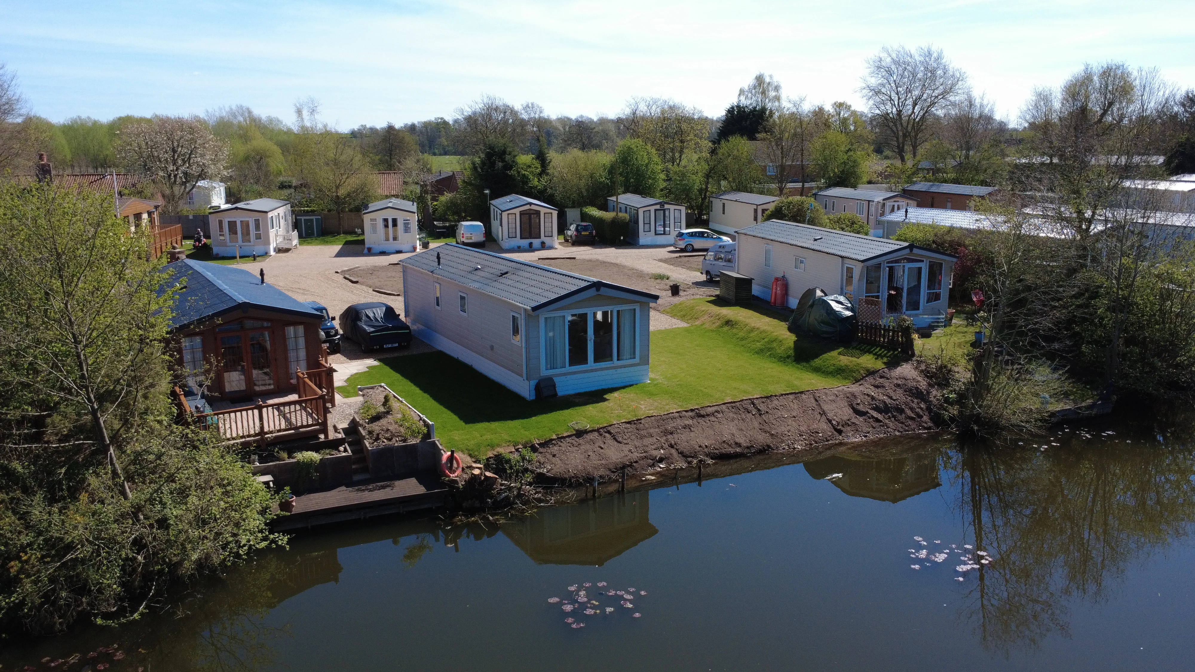 Mobile homes near calm river with trees and small wooden dock
