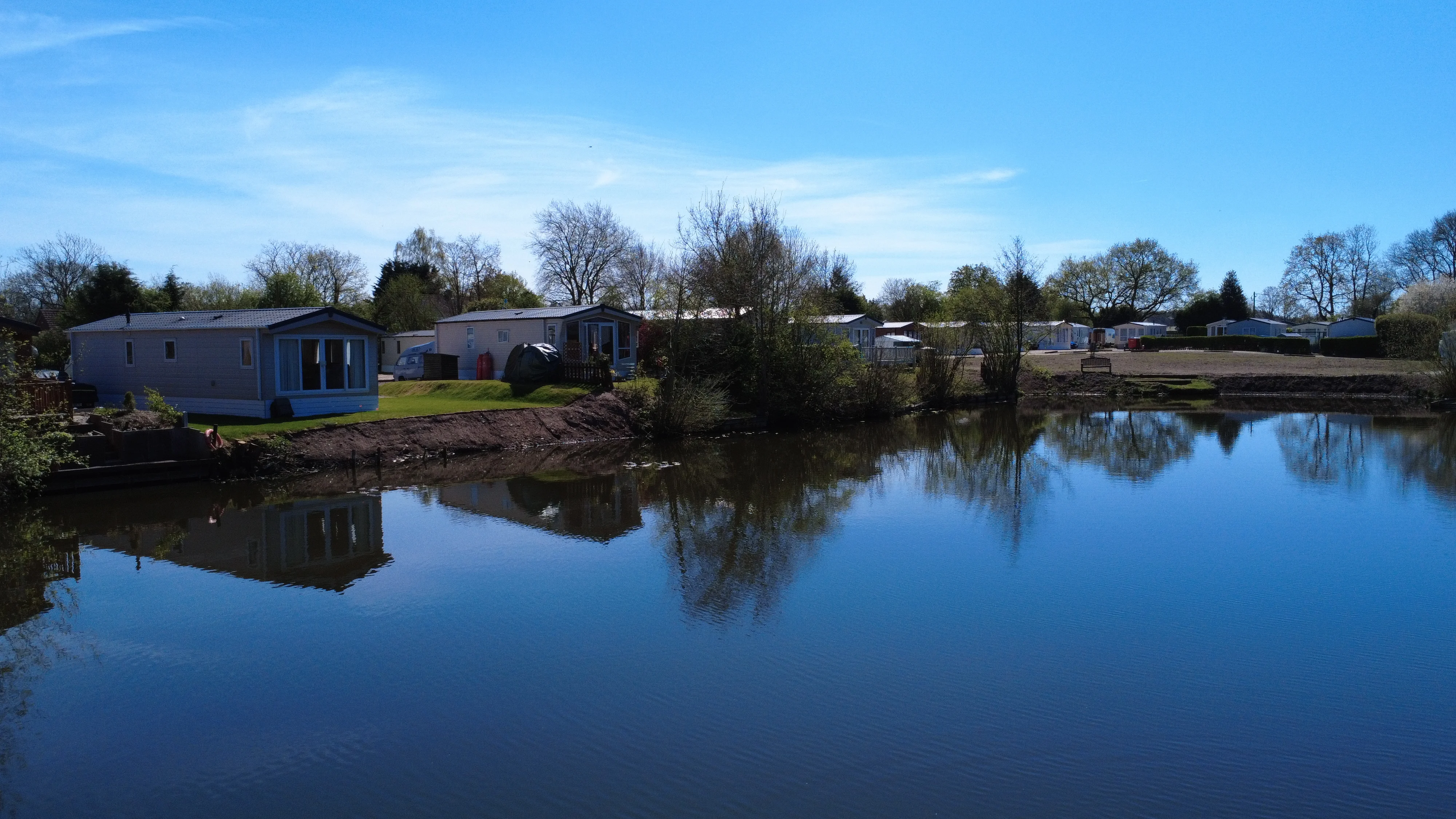 Lakeside mobile homes with trees and calm water reflecting blue sky