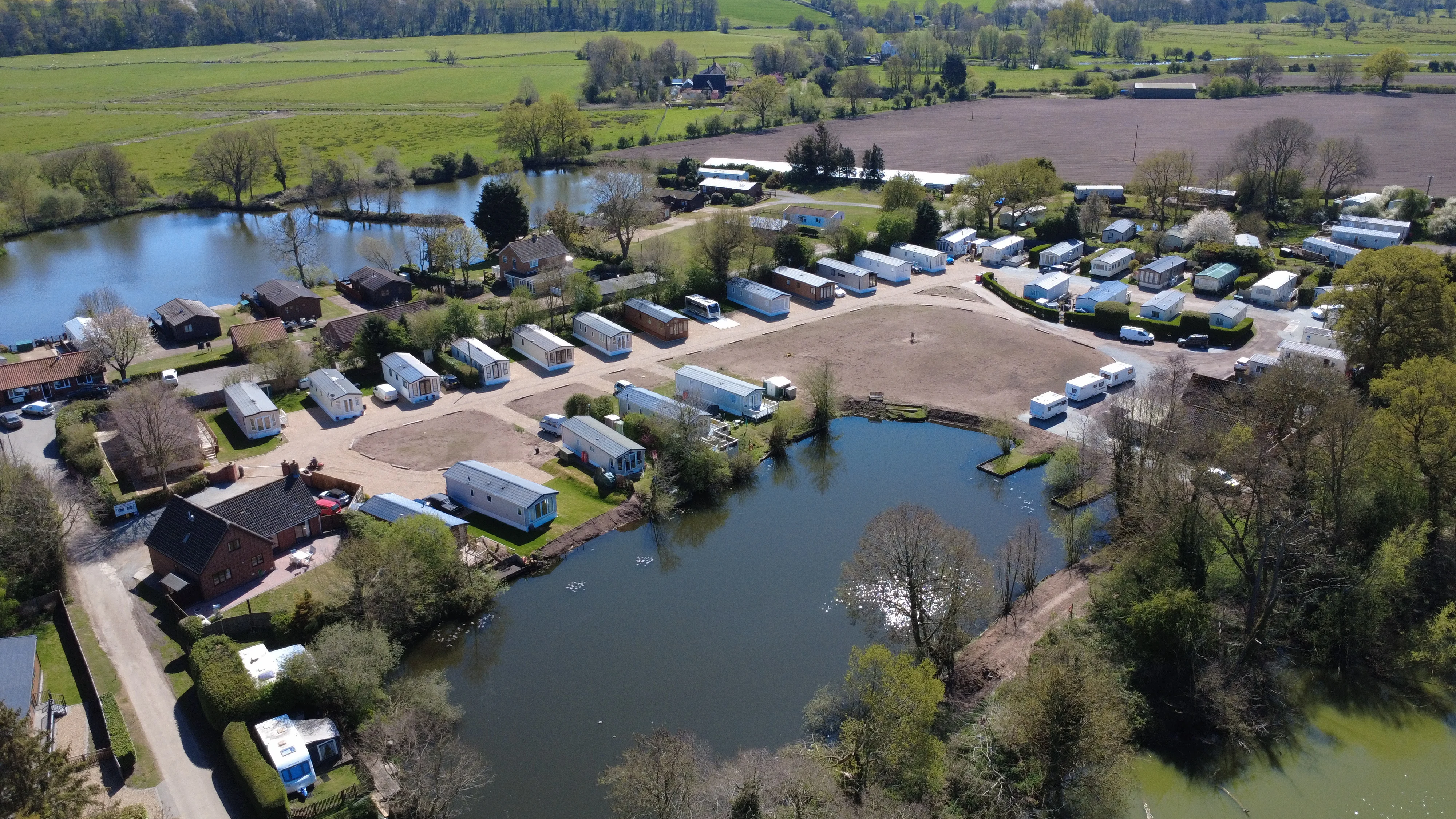 Aerial view of mobile home park with lake, trees, and green fields