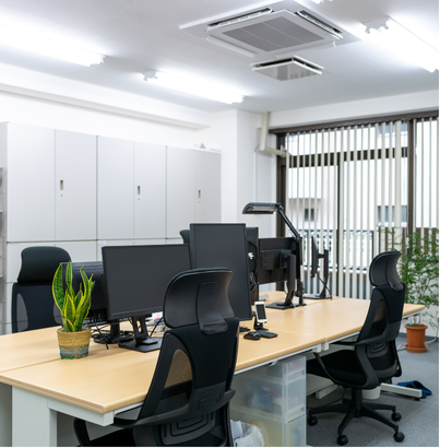Bureau moderne avec chaises de bureau noires, plusieurs écrans d'ordinateur et plantes vertes près d'une fenêtre avec stores verticaux.