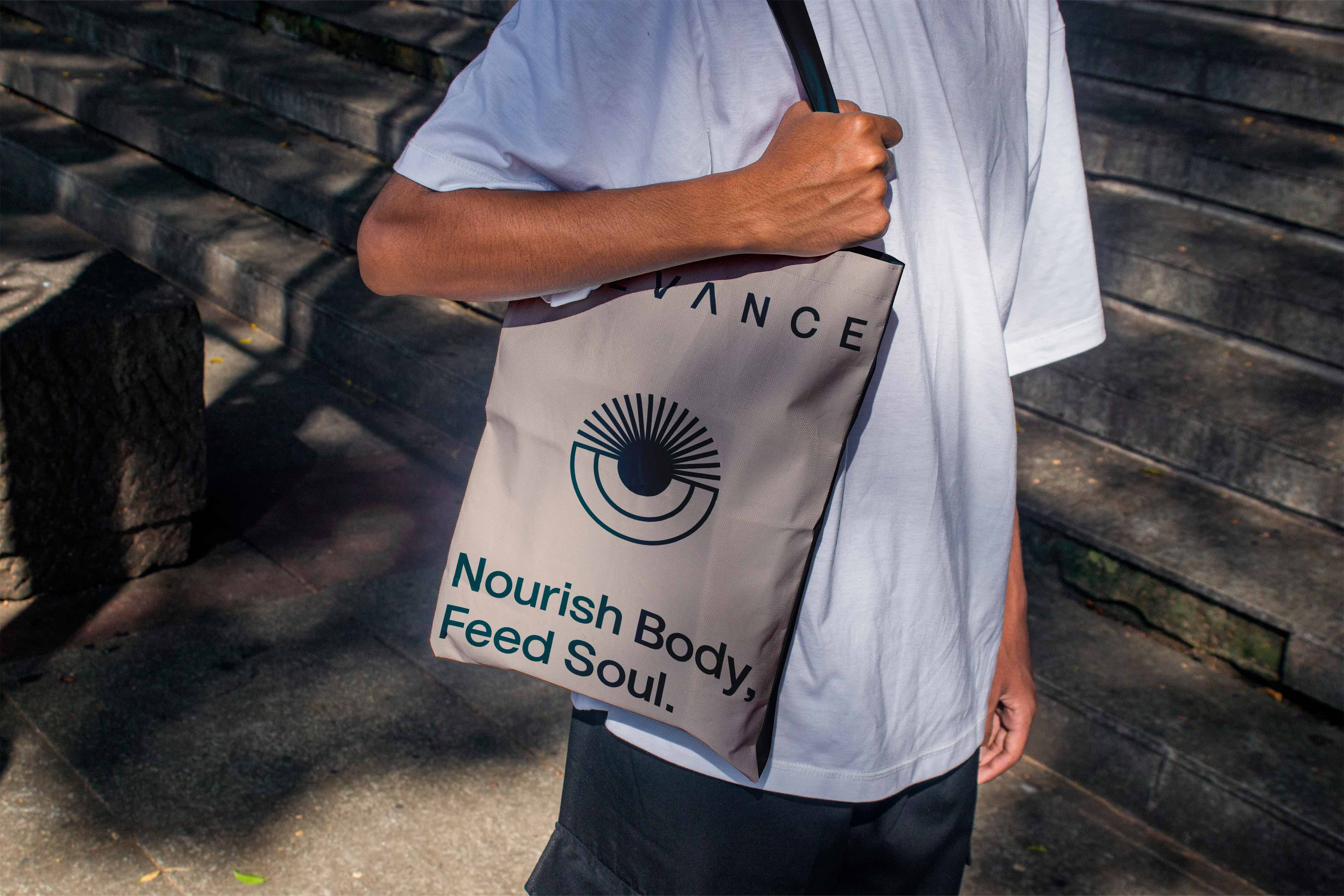 Persona con maglietta bianca porta una borsa beige con scritta Nourish Body, Feed Soul.