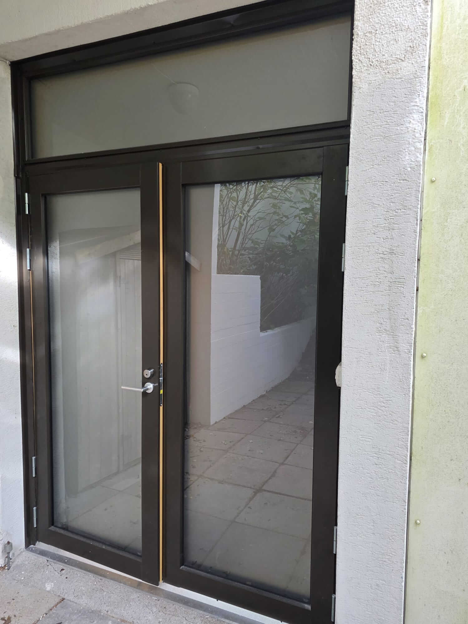 Mustat lasiovet, joiden takana näkyy valkoinen seinä ja polku, valkoisten seinien ympäröimänä.