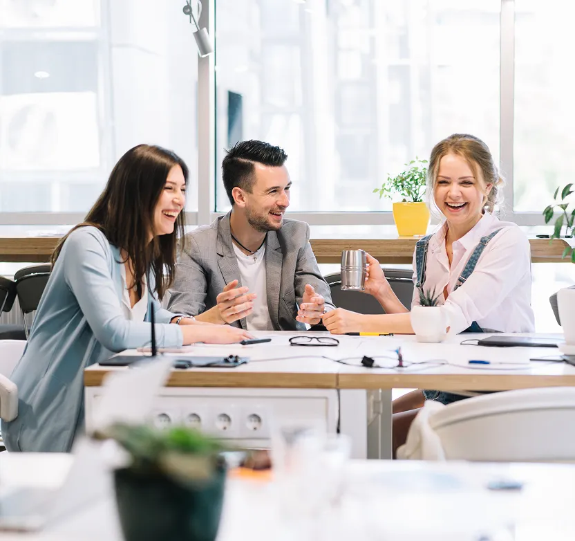 3 people sitting in office at desk and laughing