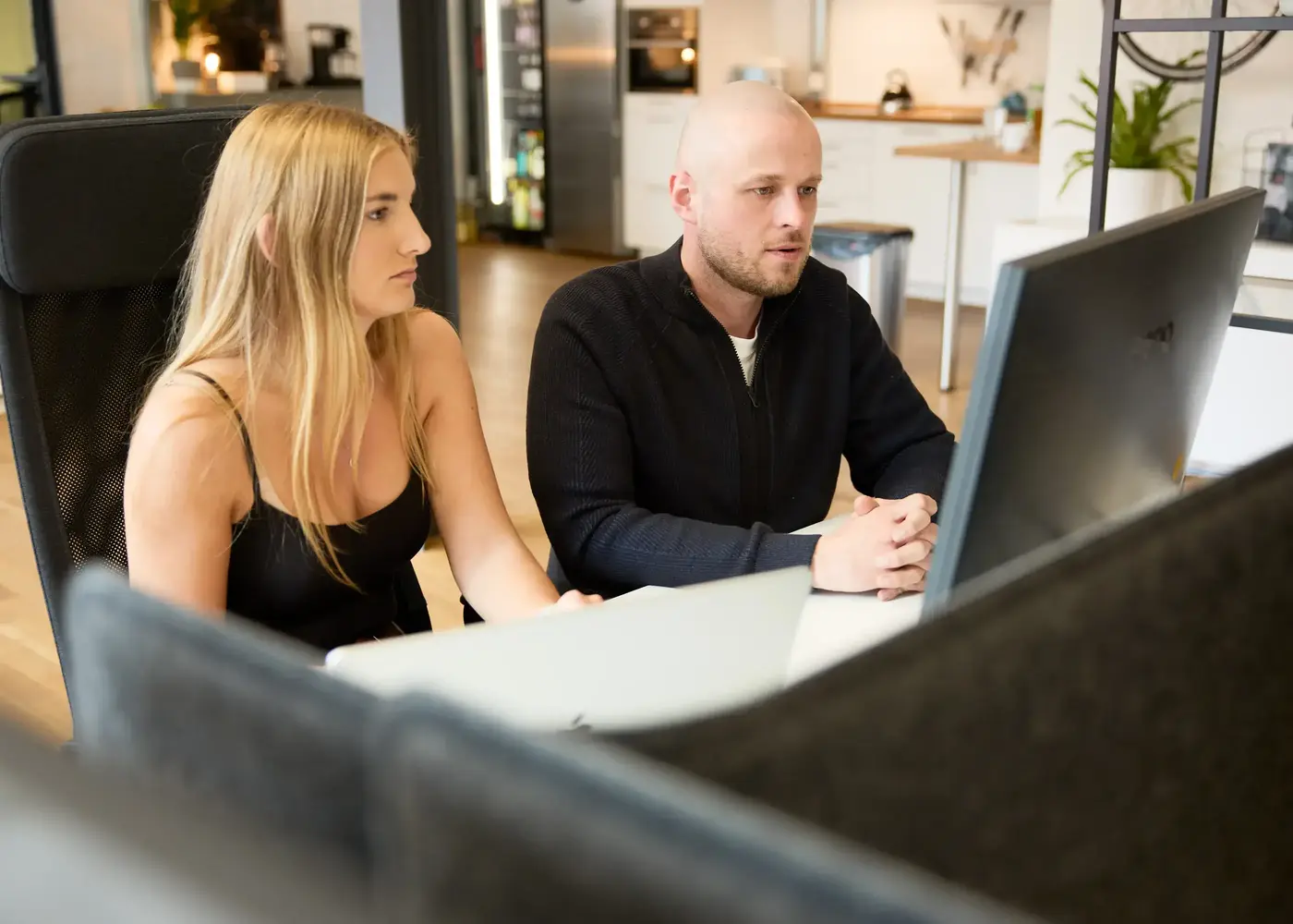 2 people sitting at desk and looking at monitor