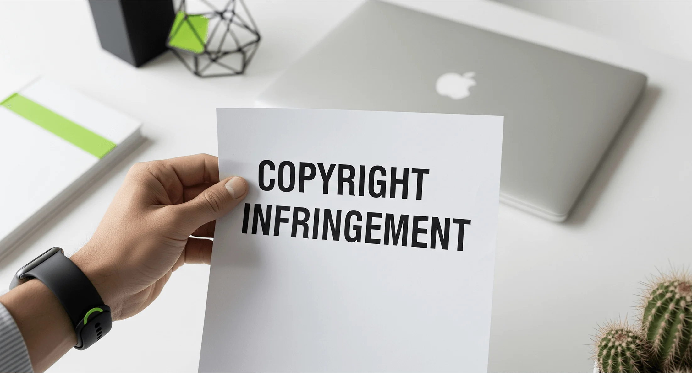Hand displaying copyright infringement paper in modern office setting with laptop and office supplies