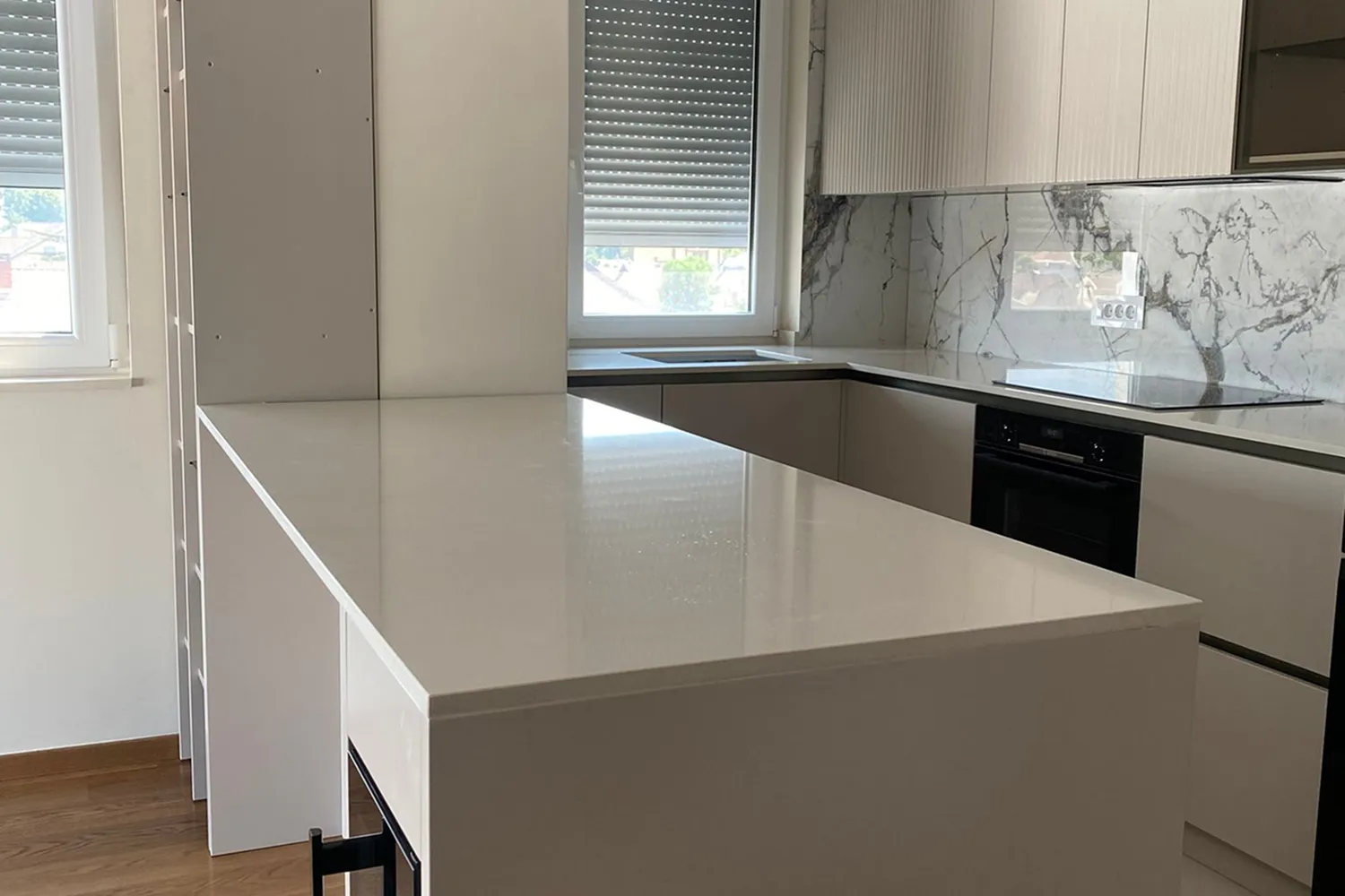 Modern kitchen with white cabinets, marble backsplash, built-in oven, and a large white island counter.