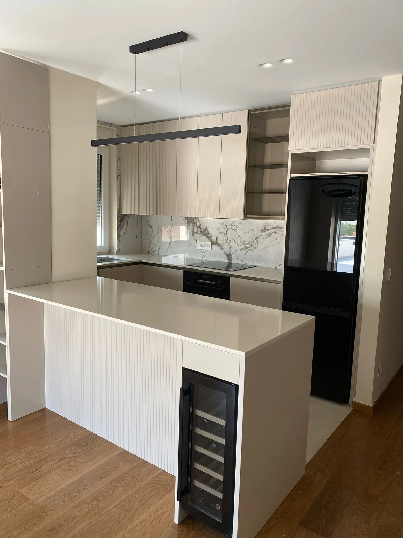 Modern kitchen with light wood cabinets, marble backsplash, black refrigerator, and white island featuring a built-in wine cooler.