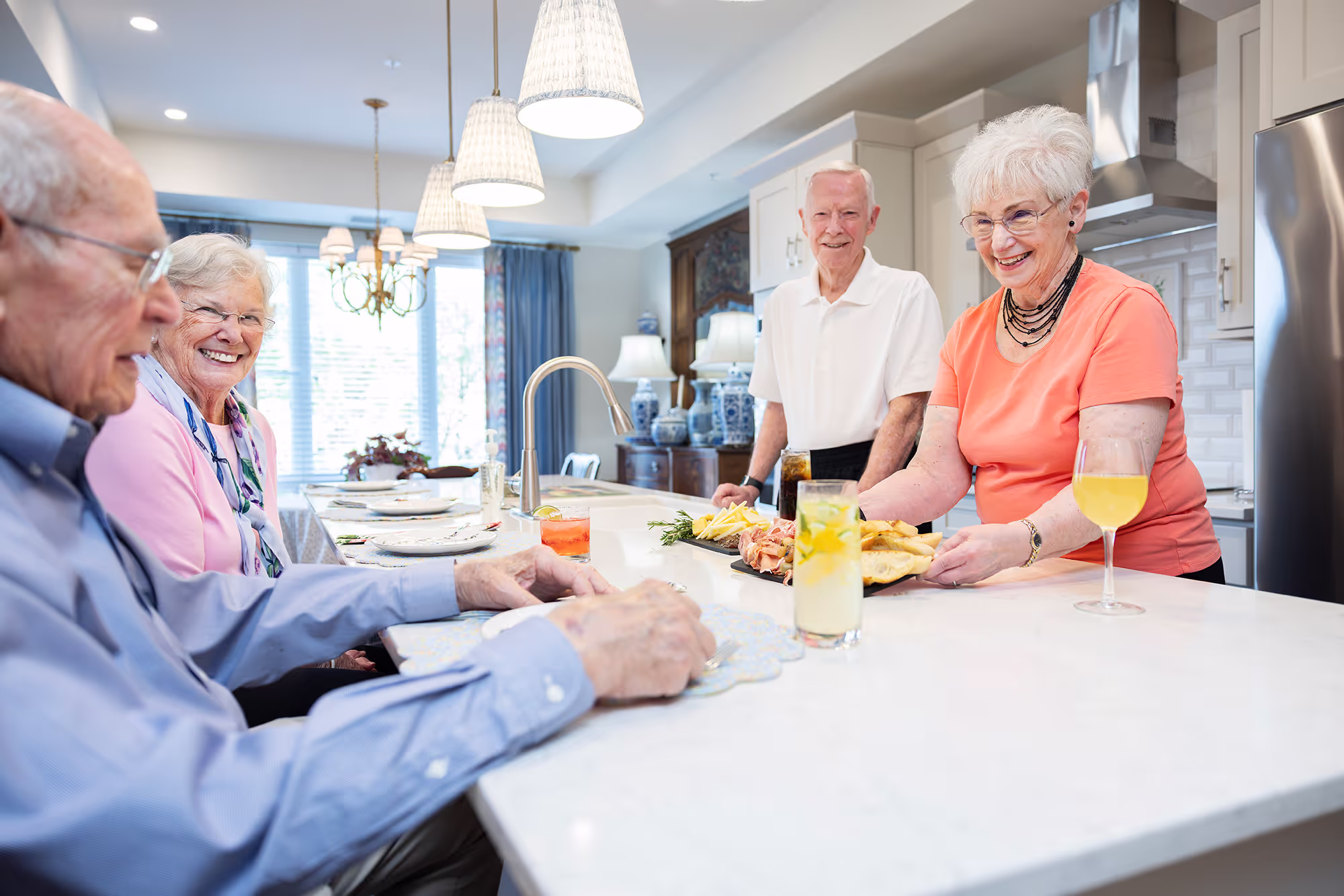 Four elderly people enjoy snacks and drinks together at a kitchen island.