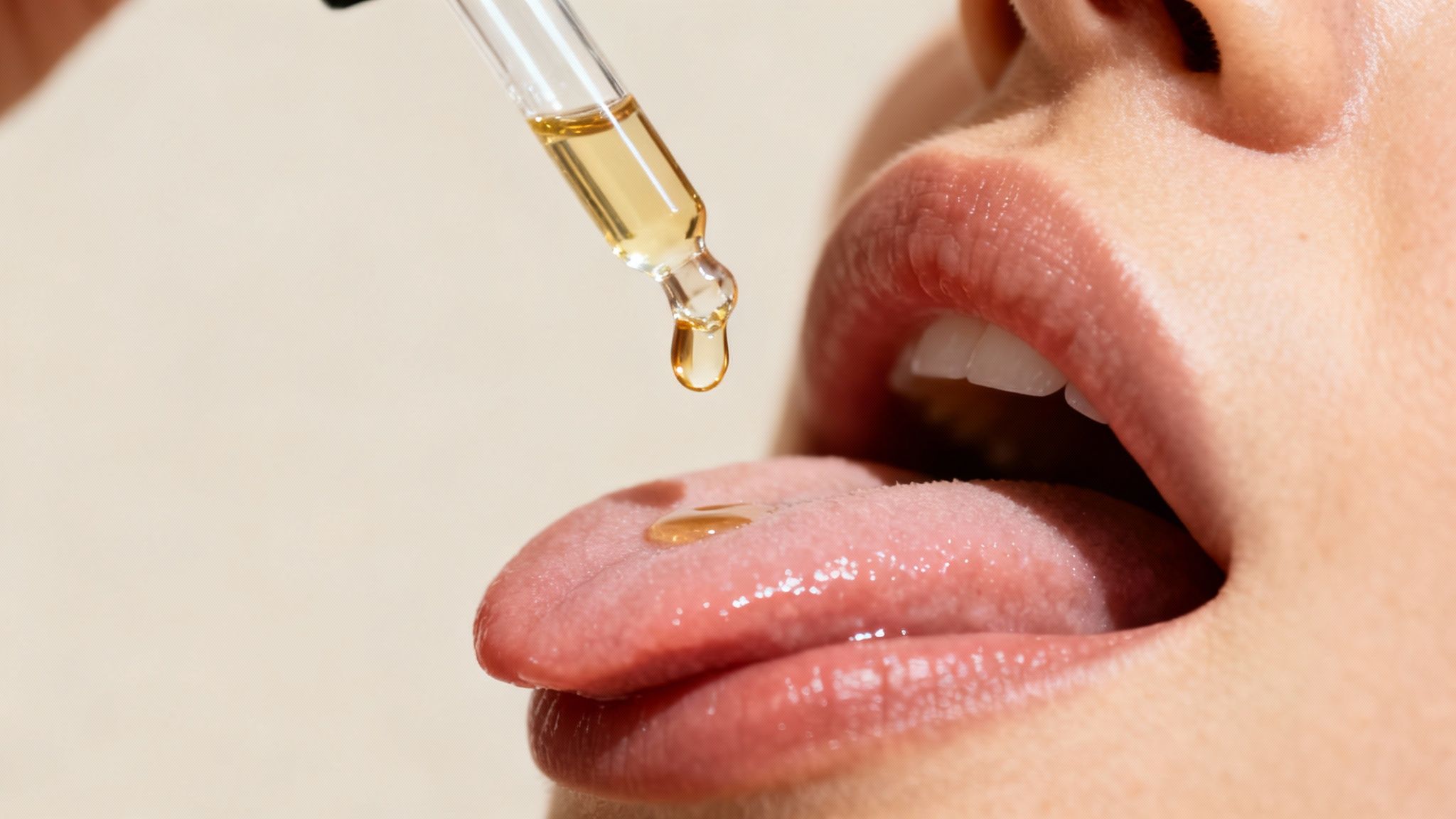 A close-up of a person's mouth with a dropper releasing a golden liquid onto their tongue.