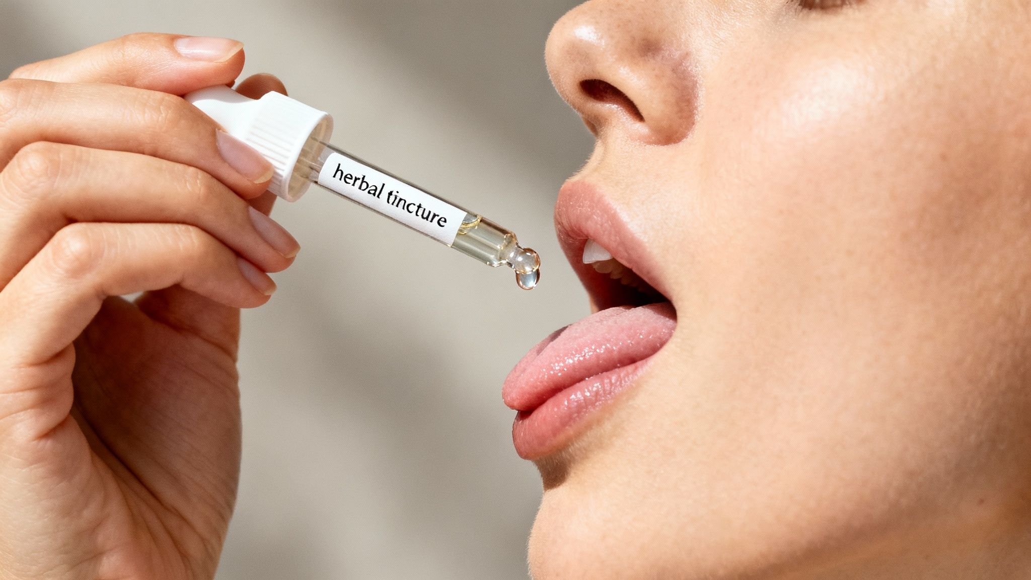 A close-up of a person's hand holding a dropper, administering herbal tincture onto their tongue.