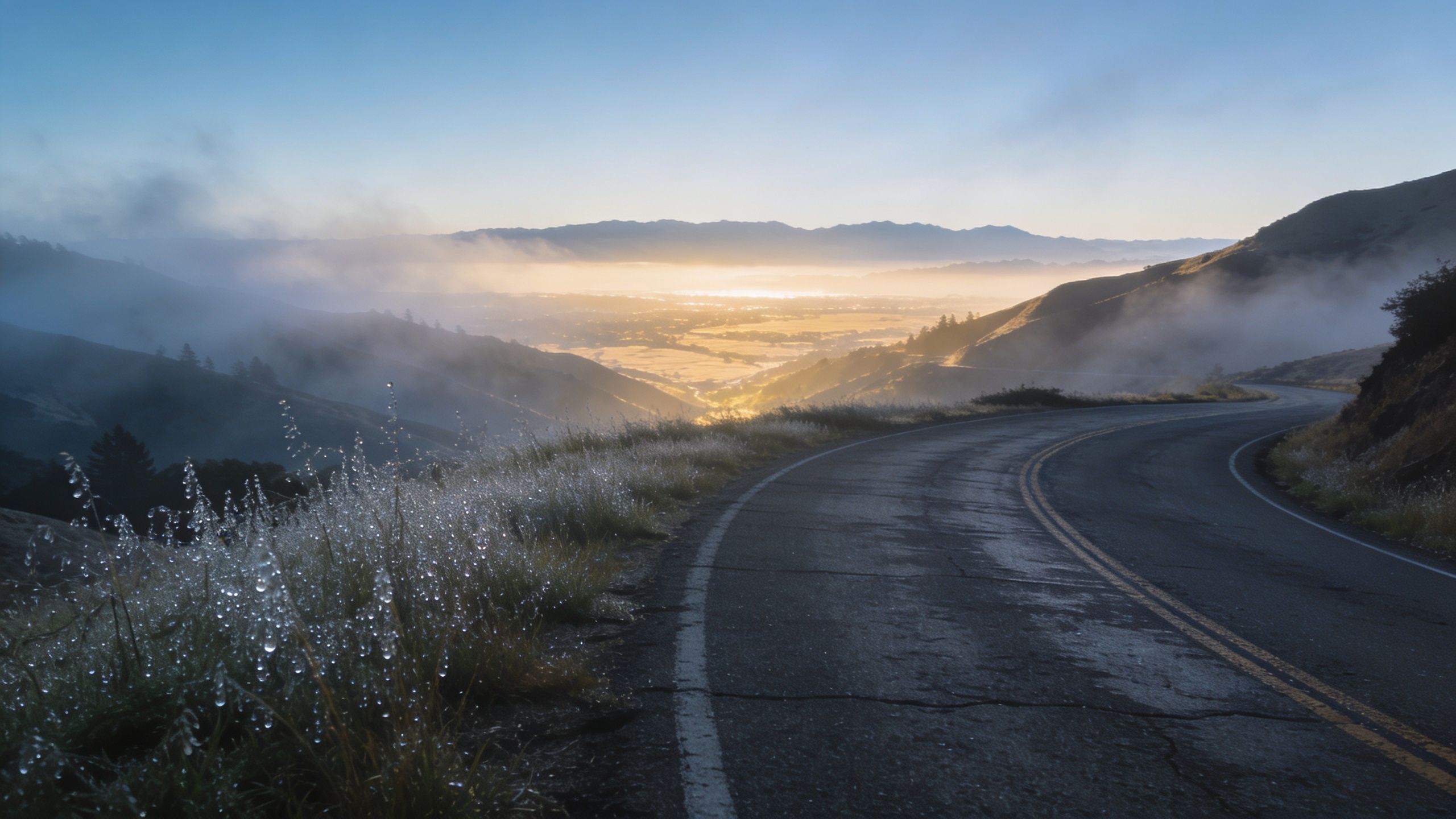 A scenic winding road overlooks a misty, sunlit valley during a beautiful morning sunrise in the mountains.