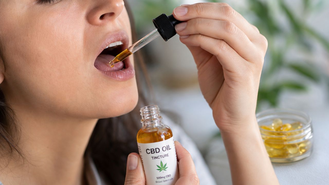 A close-up of a person administering CBD oil from a glass dropper into their mouth.