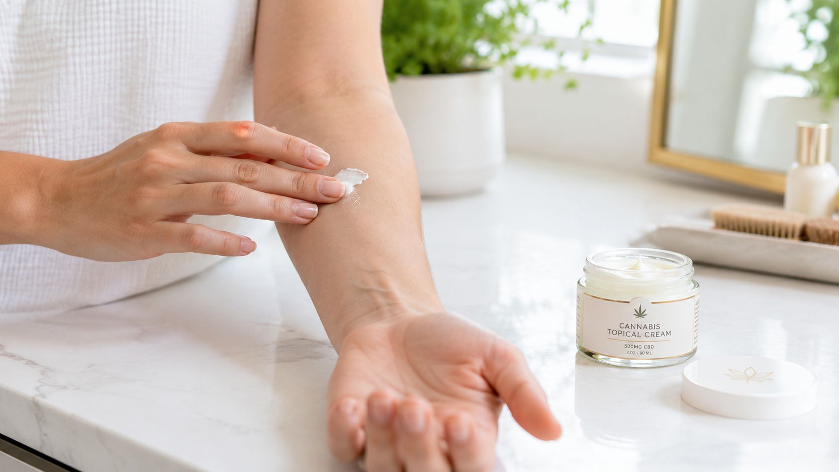 A person applying white cannabis topical cream onto their forearm on a clean marble countertop.
