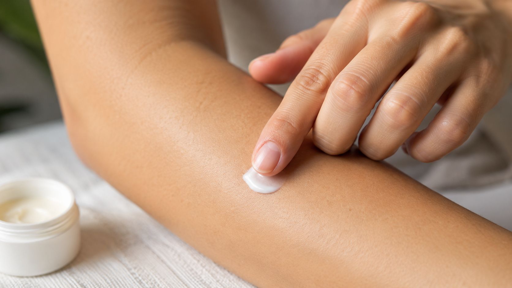 A close up of a person applying white skincare cream onto their forearm with a fingertip.