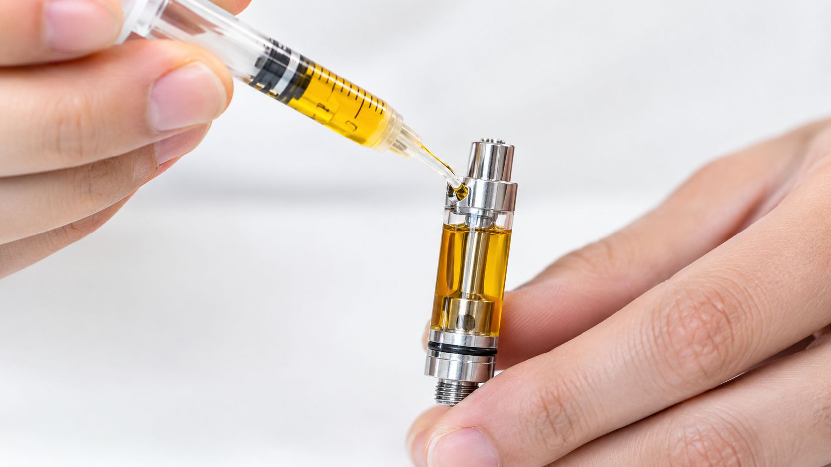 A close-up view of a person using a syringe to refill a vape pen oil cartridge.