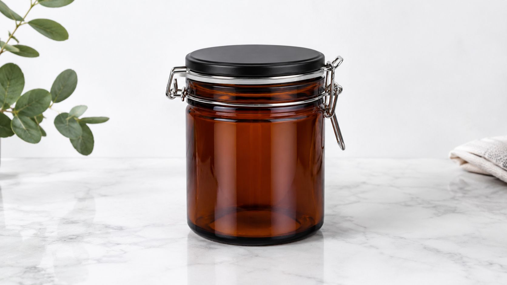 A brown glass jar with a black lid and metal latch sitting on a white marble surface.