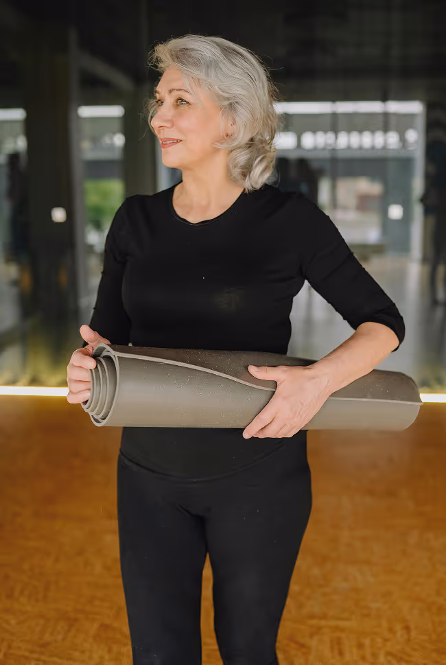 A woman holding a rolled up yoga mat.