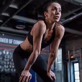 A woman in a black sports bra top and leggings squatting on a.