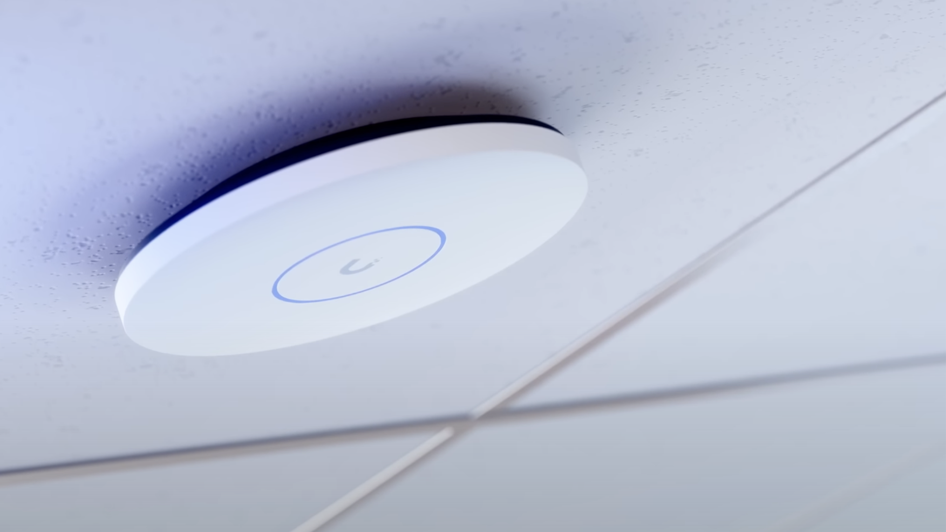 A round white network device is mounted on a ceiling with a glowing blue ring.