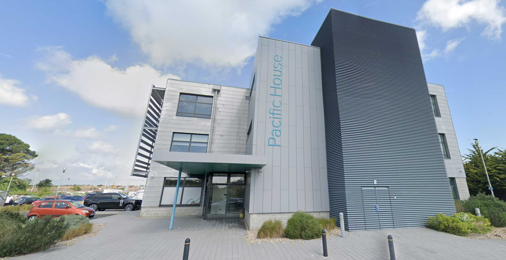 A modern office building with "Pacific House" on the exterior. Cars are parked nearby.