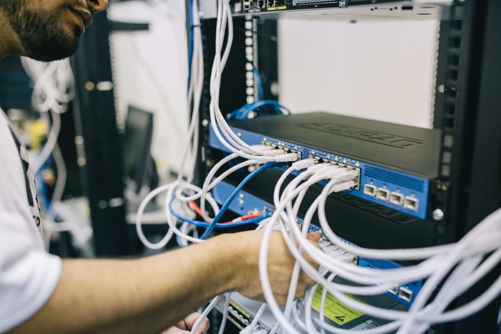 A person connects cables to a network switch in a server room.