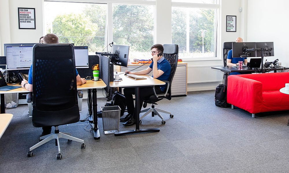 Three people sitting at desks in an office working on computers.