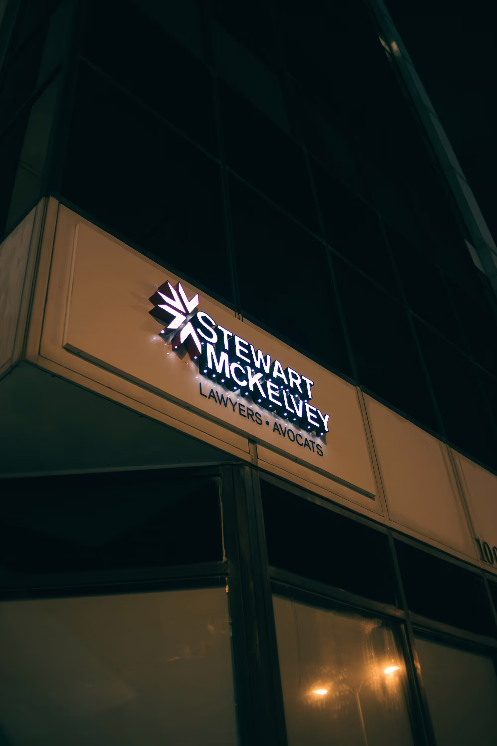 Illuminated Stewart McKelvey Lawyers Avocats sign on a building facade at night.