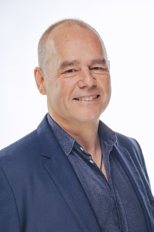 Smiling middle-aged man with short hair wearing a dark blue blazer and navy blue shirt.