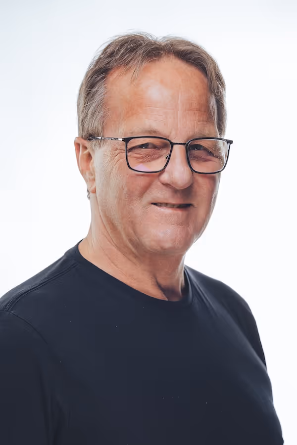 Portrait of an older man with glasses wearing a black shirt against a white background.