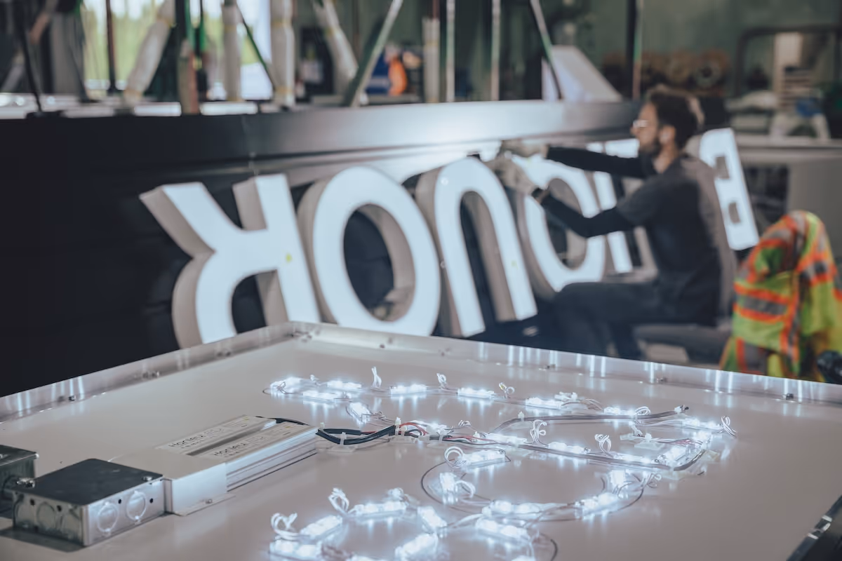 Person assembling illuminated letters with LED wiring on a work table in a workshop.