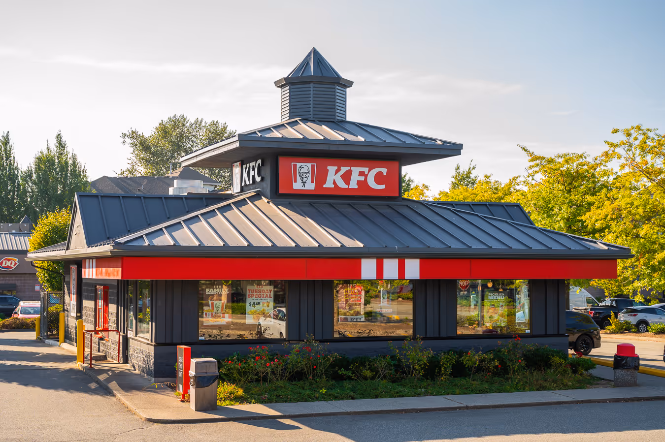 KFC restaurant building with a dark gray roof and red signage under a partly cloudy sky.