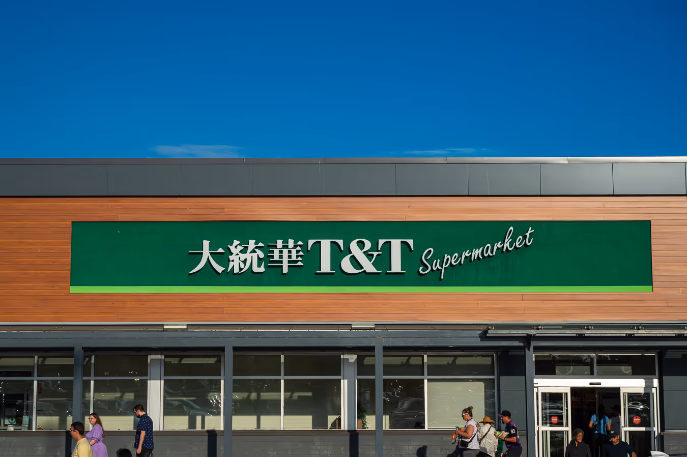 Exterior of a T&T Supermarket with a large green sign and people walking in front.