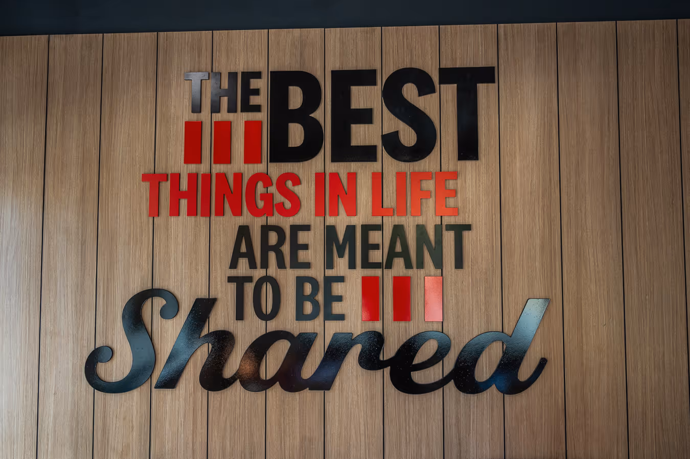 Wall display with the text 'The best things in life are meant to be shared' in black and red letters on a wooden background.