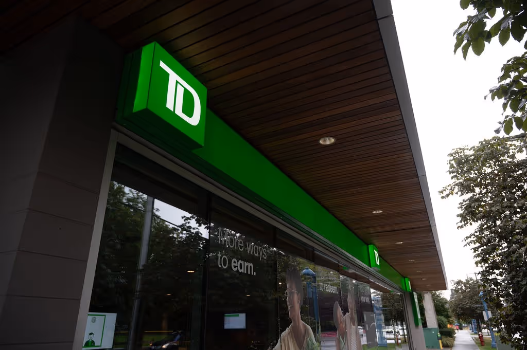 Exterior of a TD bank branch with green signage under a wooden canopy on a city sidewalk.