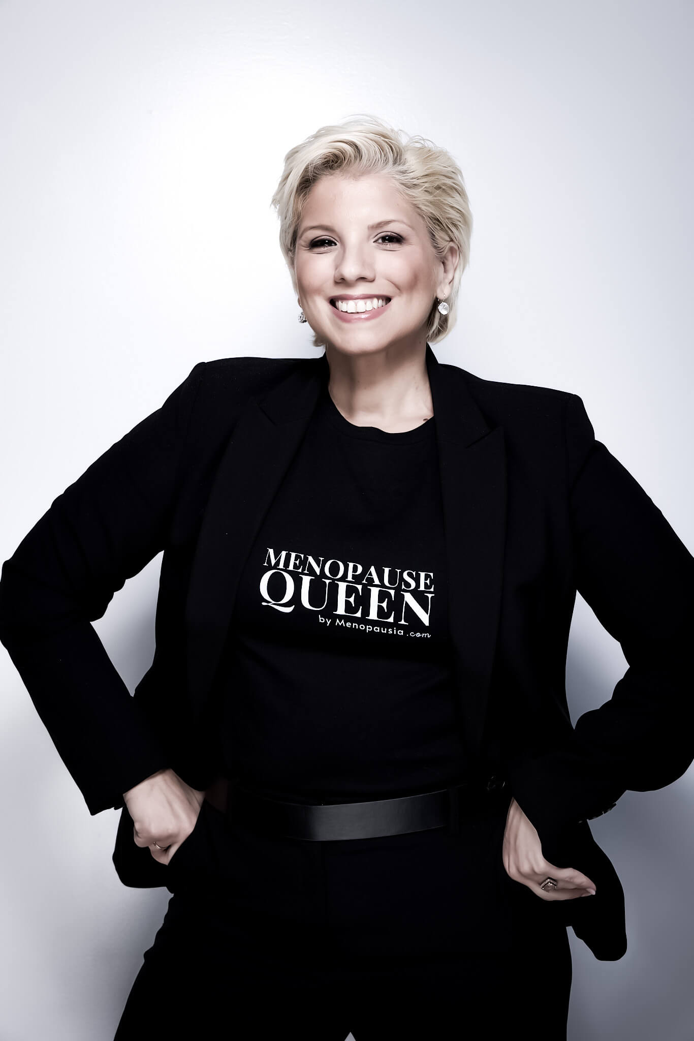 Smiling woman with short blonde hair wearing black blazer and a shirt that reads 'Menopause Queen by Menopausia.com'.