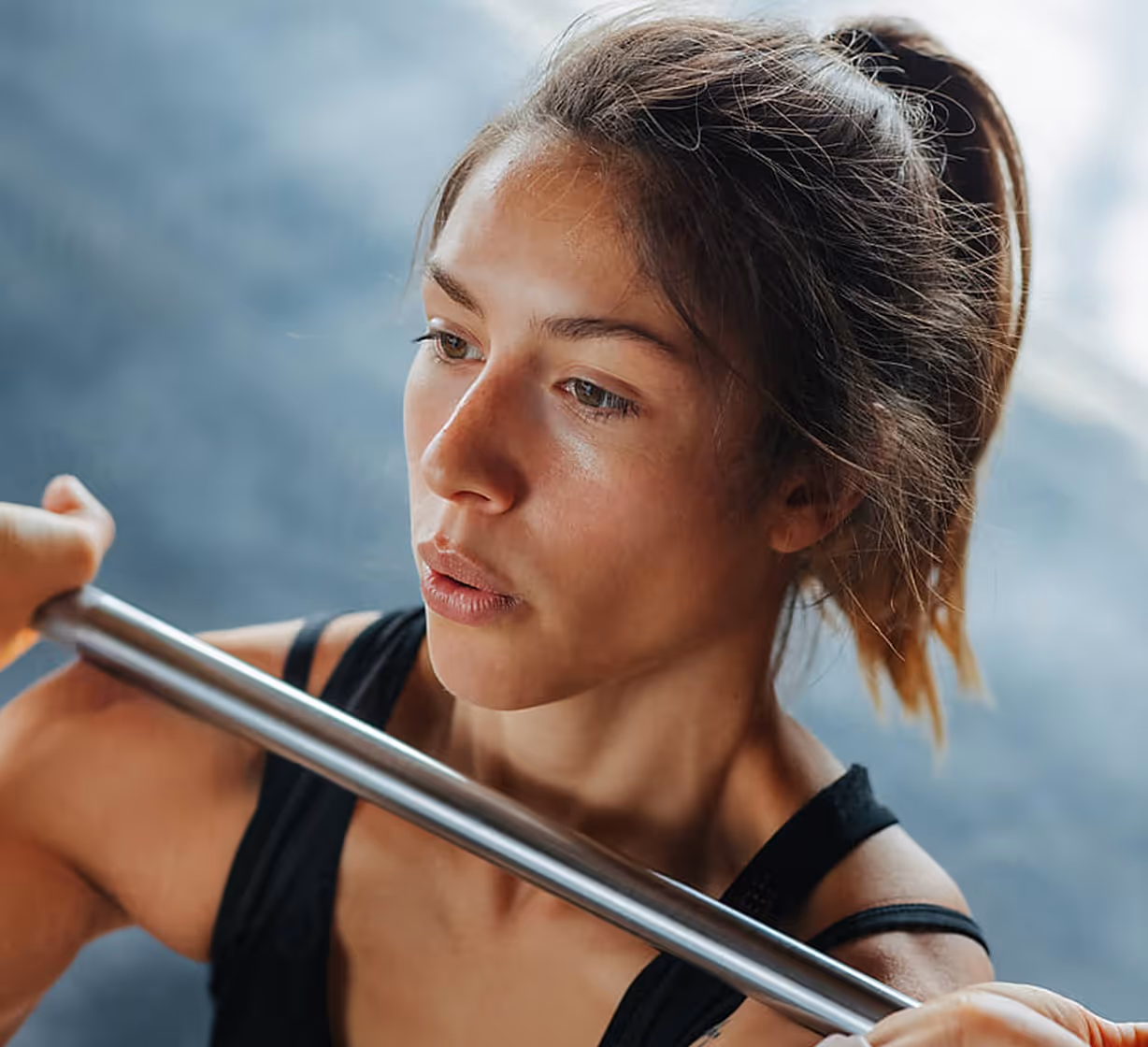 Focused woman holding a metal barbell across her shoulders during a workout.