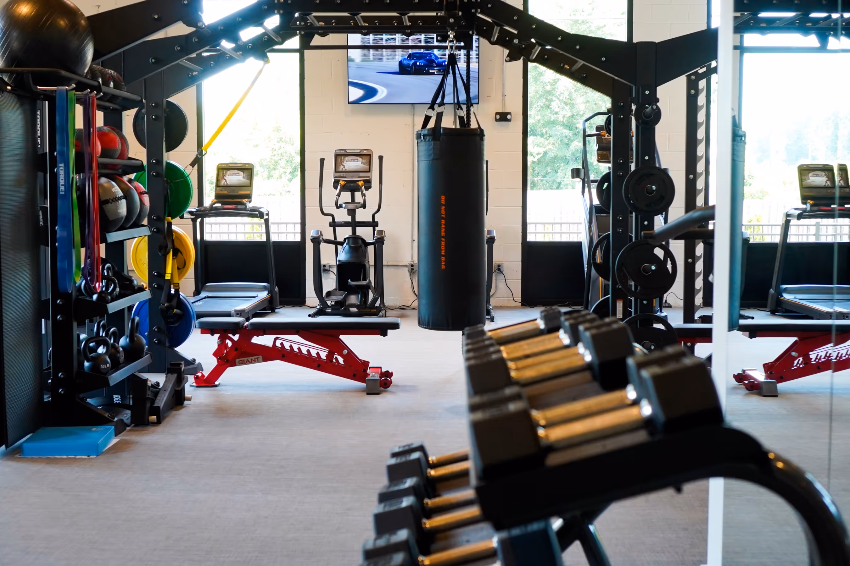 Modern gym interior with dumbbells, weight bench, kettlebells, resistance bands, punching bag, treadmill, and exercise bike.