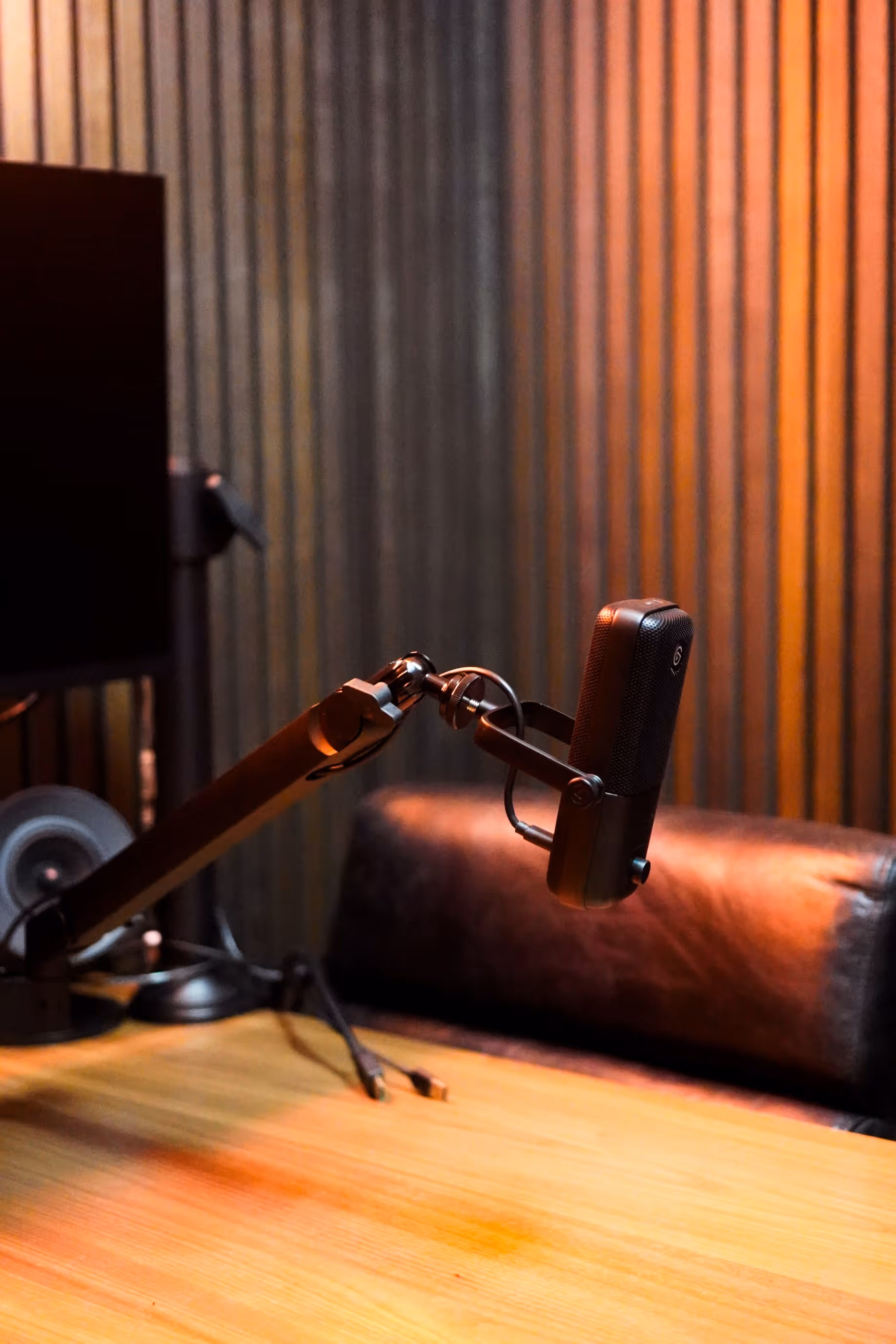 Black microphone mounted on an adjustable arm over a wooden desk in a room with striped wall panels and a leather chair.
